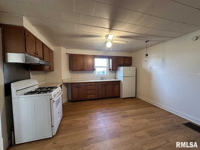 kitchen featuring under cabinet range hood, white appliances, wood finished floors, a sink, and backsplash