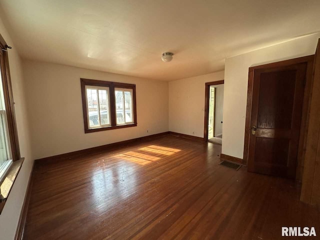 unfurnished room featuring visible vents, dark wood finished floors, and baseboards