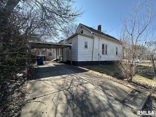 view of property exterior featuring concrete driveway, a carport, and a chimney
