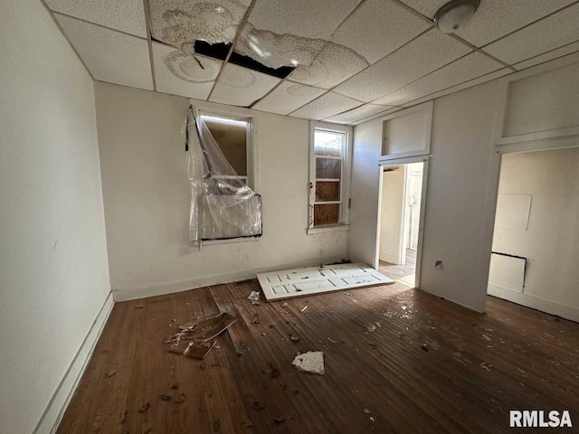 unfurnished bedroom with baseboards, a drop ceiling, and hardwood / wood-style floors