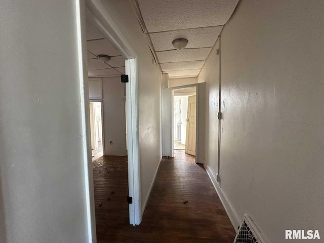 hall featuring a paneled ceiling, dark wood-style floors, baseboards, and visible vents