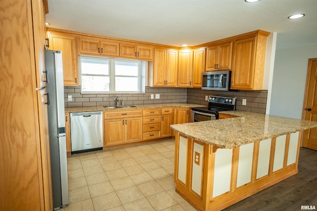 kitchen featuring light stone counters, stainless steel appliances, backsplash, a sink, and a peninsula