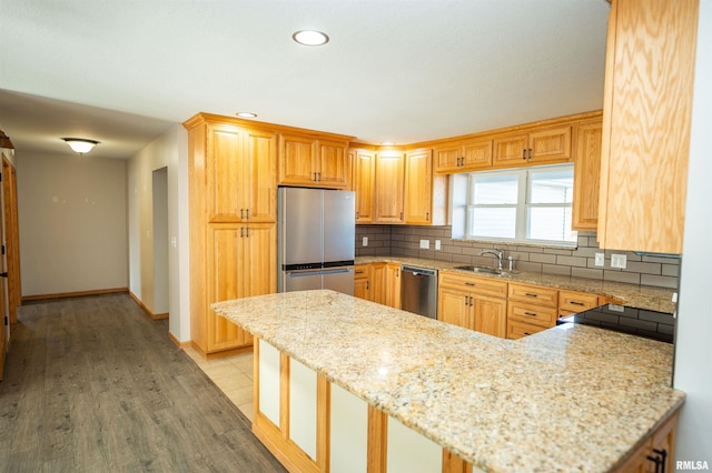kitchen featuring baseboards, a peninsula, stainless steel appliances, light wood-style floors, and backsplash
