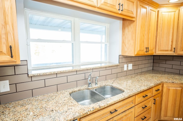 kitchen with light stone counters, a sink, and decorative backsplash