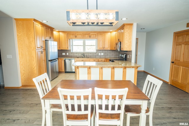 kitchen featuring decorative backsplash, appliances with stainless steel finishes, a sink, light wood-type flooring, and a peninsula