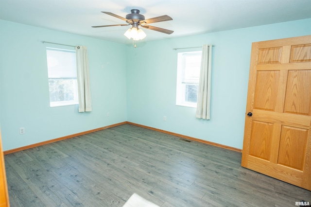 spare room with a ceiling fan, visible vents, baseboards, and wood finished floors