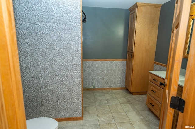 bathroom featuring wainscoting, toilet, and wallpapered walls