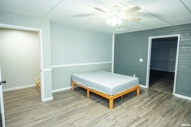 bedroom featuring a drop ceiling, ceiling fan, baseboards, and wood finished floors