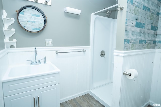 bathroom featuring vanity, walk in shower, wood finished floors, and wainscoting