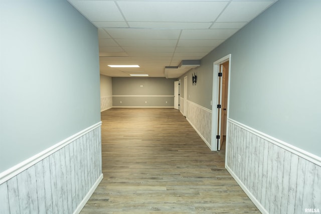 hallway featuring wainscoting, a drop ceiling, and wood finished floors