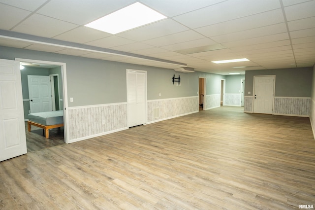 empty room featuring a wainscoted wall, a drop ceiling, and wood finished floors