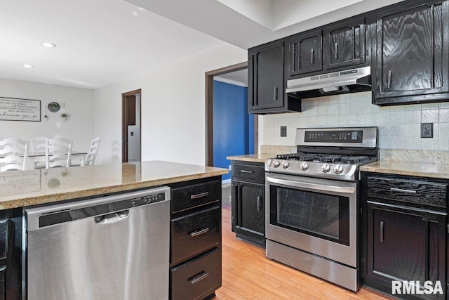 kitchen featuring stainless steel appliances, tasteful backsplash, dark cabinets, light wood-type flooring, and under cabinet range hood