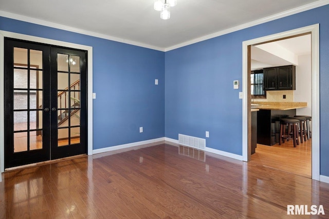 spare room with french doors, crown molding, visible vents, wood finished floors, and baseboards