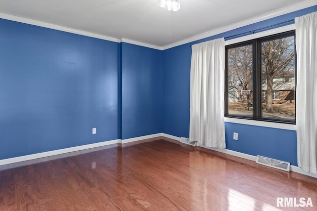 empty room featuring ornamental molding, visible vents, baseboards, and wood finished floors