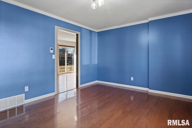 empty room featuring baseboards, visible vents, wood finished floors, and ornamental molding