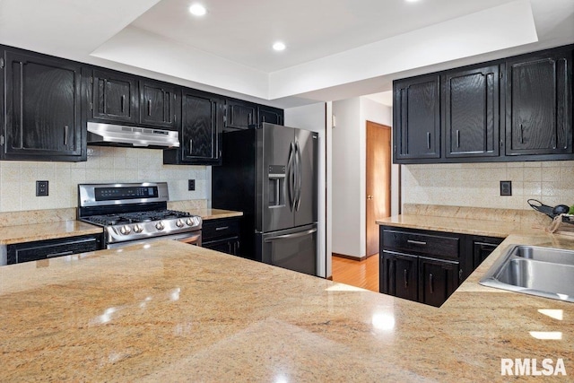 kitchen featuring decorative backsplash, appliances with stainless steel finishes, dark cabinets, under cabinet range hood, and a sink