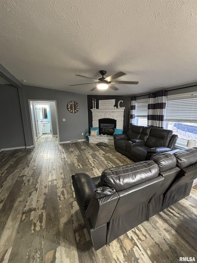 living area with baseboards, a ceiling fan, wood finished floors, a textured ceiling, and a fireplace