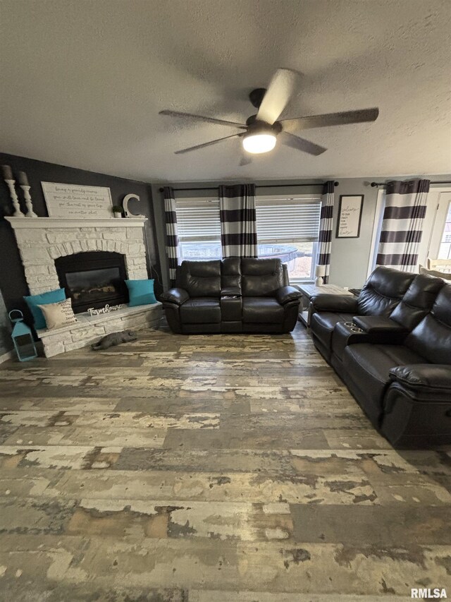 living area with a textured ceiling, a fireplace, a ceiling fan, and wood finished floors