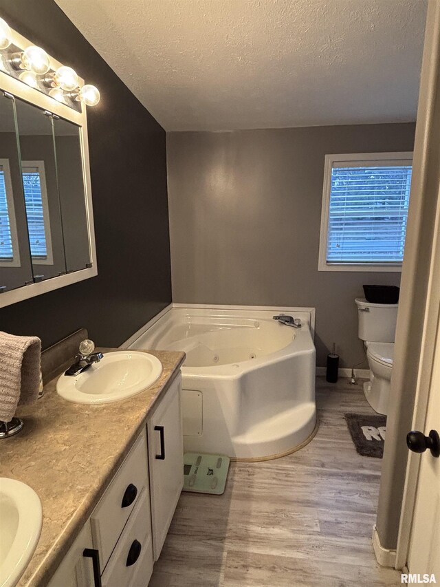 full bath featuring a textured ceiling, toilet, wood finished floors, a sink, and a whirlpool tub