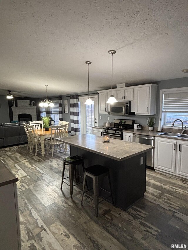 kitchen featuring a large fireplace, stainless steel appliances, a kitchen island, a sink, and white cabinets