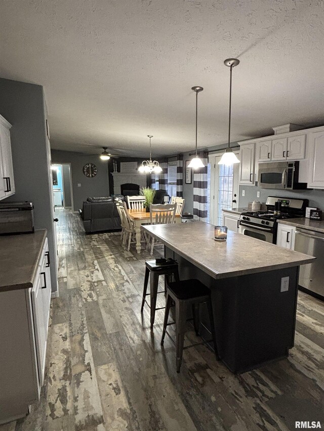 kitchen featuring dark wood finished floors, stainless steel appliances, white cabinets, a kitchen island, and a textured ceiling