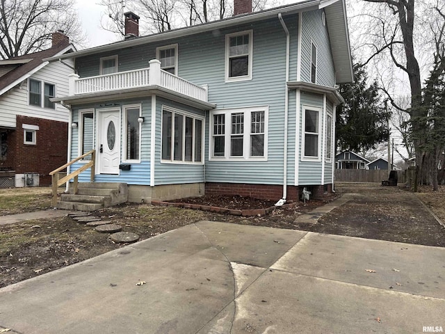 view of front of house with a balcony, a chimney, and entry steps