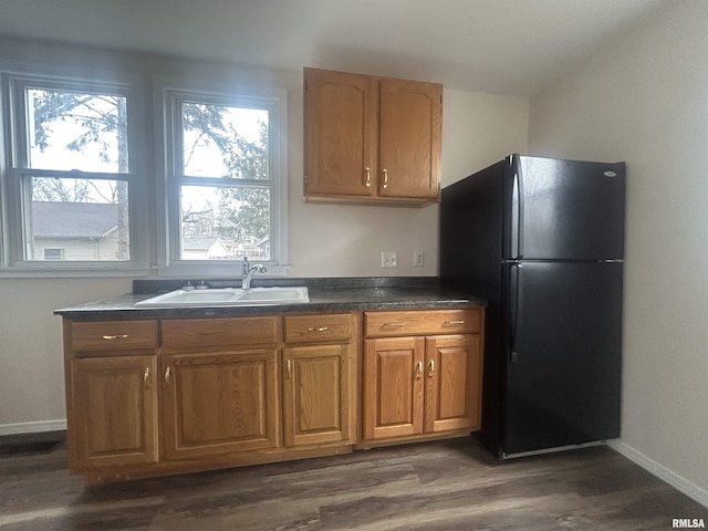 kitchen with dark wood-style flooring, brown cabinets, dark countertops, freestanding refrigerator, and a sink