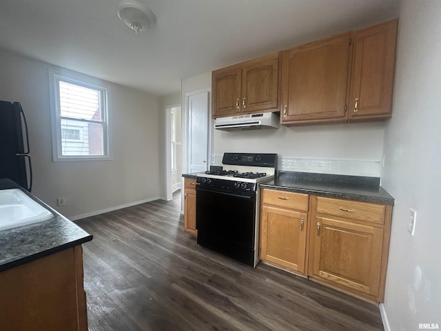 kitchen featuring exhaust hood, dark countertops, freestanding refrigerator, and range with gas cooktop