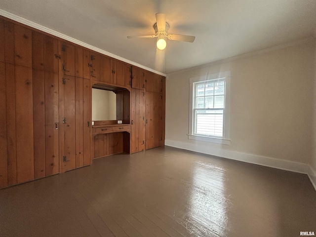 empty room with baseboards, a ceiling fan, wood finished floors, crown molding, and wood walls