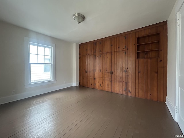 spare room featuring built in shelves, dark wood-style flooring, and baseboards