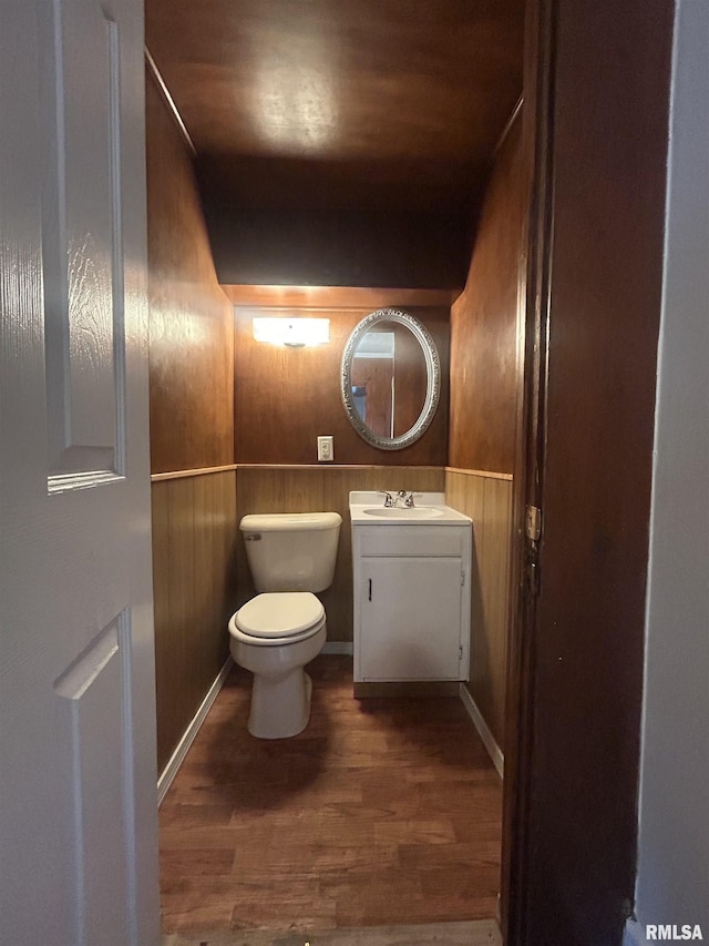 half bath featuring toilet, wooden walls, wood finished floors, and vanity