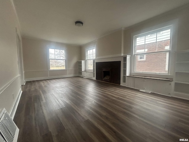 unfurnished living room with dark wood-style flooring, a fireplace, visible vents, baseboards, and ornamental molding