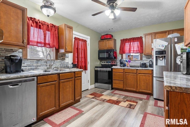 kitchen featuring stainless steel appliances, light wood finished floors, a sink, and brown cabinets