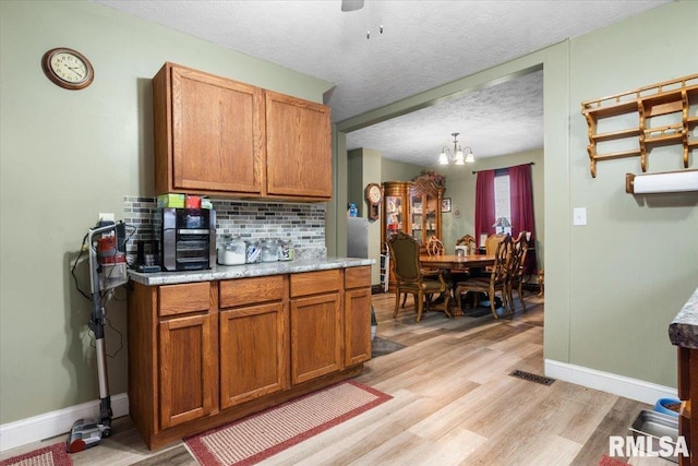 kitchen with brown cabinets, light wood finished floors, tasteful backsplash, light countertops, and a textured ceiling