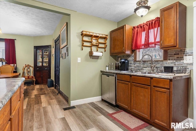 kitchen featuring light wood finished floors, baseboards, decorative backsplash, dishwasher, and a sink