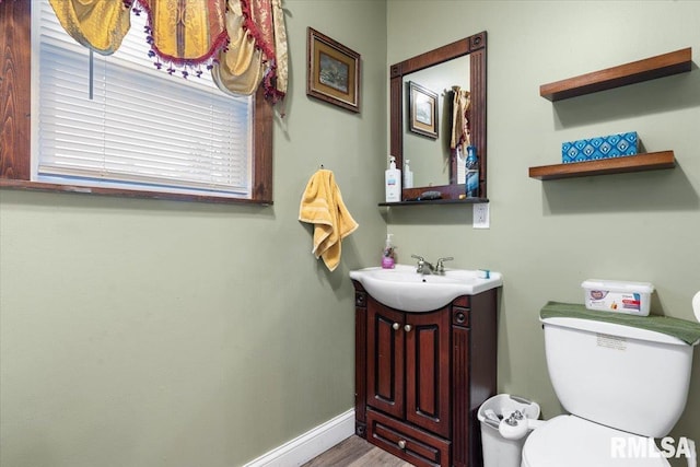 half bath with toilet, baseboards, and vanity