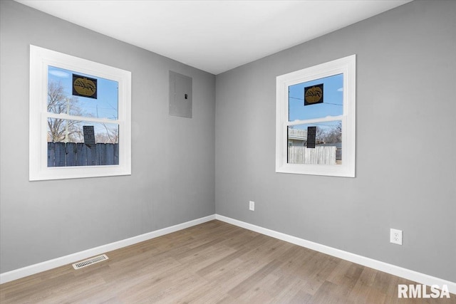 empty room with electric panel, visible vents, light wood finished floors, and baseboards