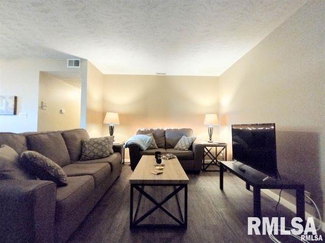 living room featuring dark wood-type flooring, visible vents, and a textured ceiling