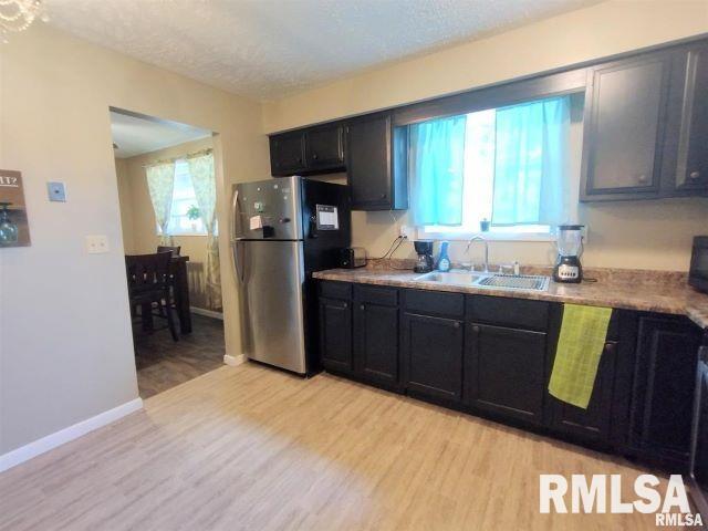 kitchen with dark cabinets, a sink, light countertops, light wood-type flooring, and freestanding refrigerator