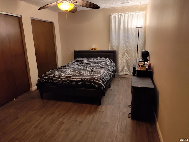 bedroom featuring baseboards, two closets, a textured ceiling, and wood finished floors