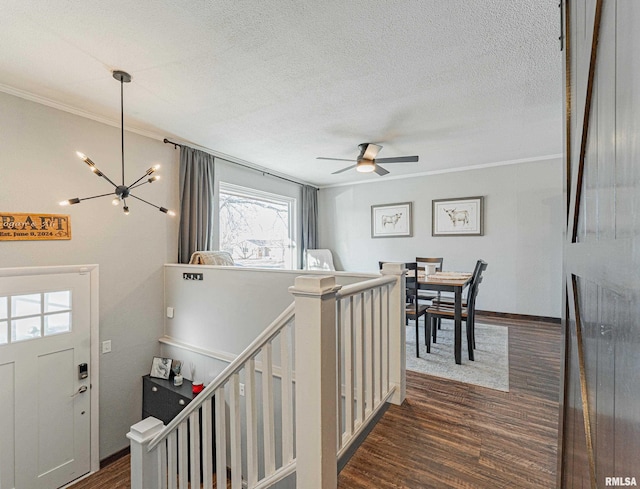 hall featuring a notable chandelier, dark wood finished floors, ornamental molding, a textured ceiling, and an upstairs landing