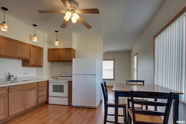 kitchen featuring decorative light fixtures, brown cabinetry, light wood-style floors, a sink, and white appliances