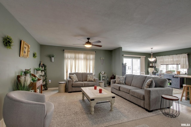 living area with light carpet, ceiling fan, baseboards, and a textured ceiling