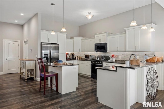 kitchen with dark wood-style flooring, decorative backsplash, black appliances, white cabinetry, and a kitchen breakfast bar