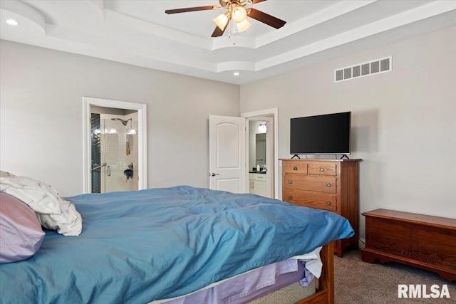 bedroom featuring visible vents, a tray ceiling, ensuite bath, carpet flooring, and ceiling fan