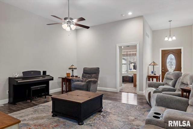 living area featuring ceiling fan with notable chandelier, wood finished floors, and baseboards