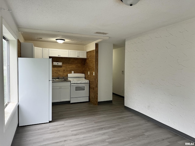 kitchen with a textured wall, light wood-style flooring, white appliances, a sink, and visible vents