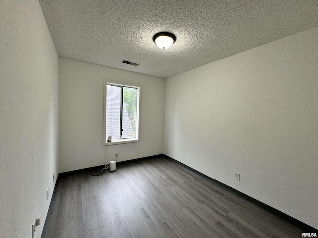 unfurnished room with baseboards, visible vents, dark wood finished floors, and a textured ceiling