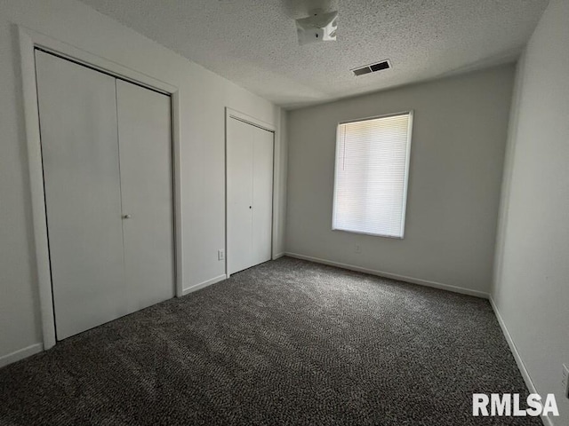 unfurnished bedroom with carpet floors, two closets, visible vents, a textured ceiling, and baseboards