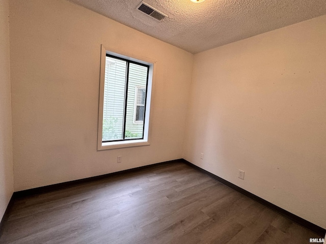 empty room with baseboards, a textured ceiling, visible vents, and dark wood-style flooring